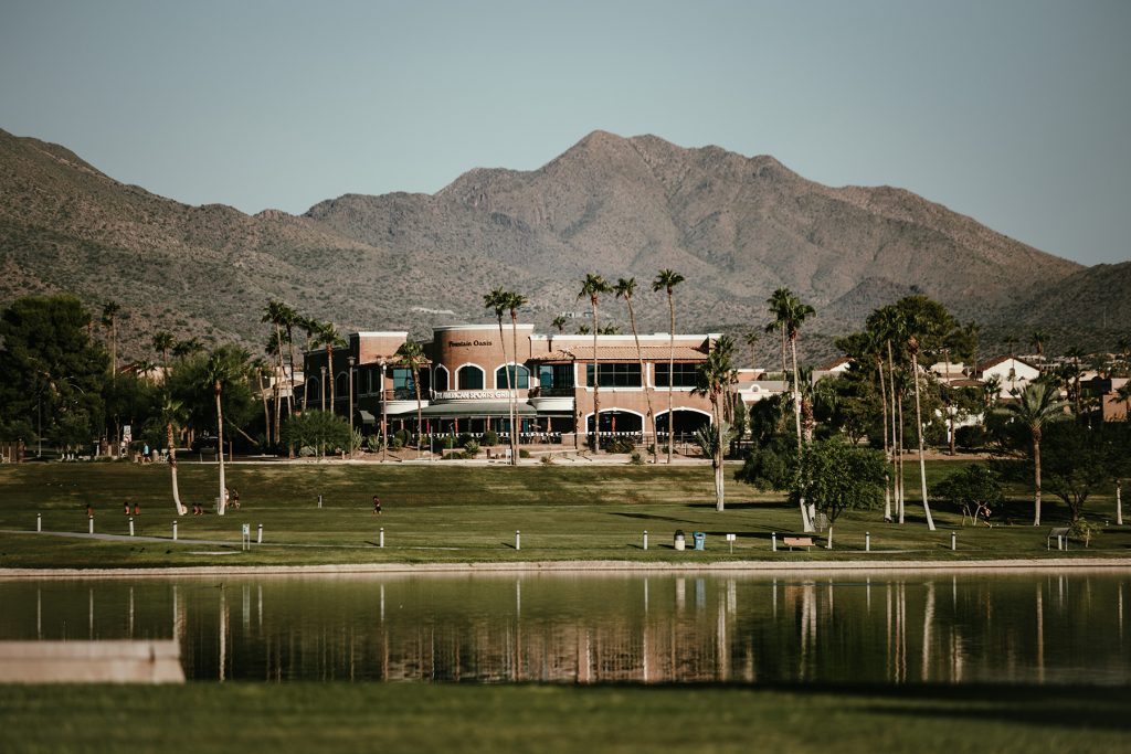 A view of Fountain Hills, Arizona, with a bustling city, historic reservation, and a prominent man-made geyser in a lush green park.