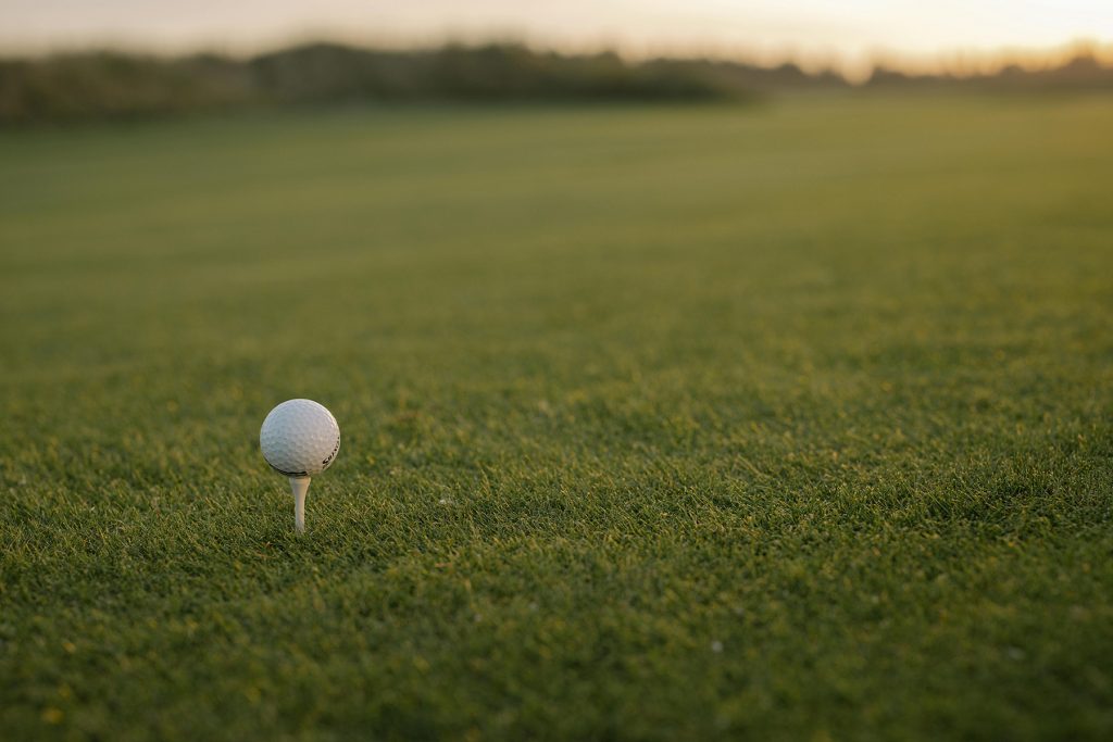 View of golf ball on a tee with lush green fairway, with the sun setting a staple of fountain hills golfing