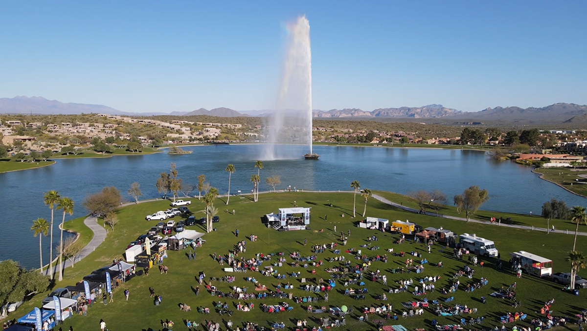 Joyful atmosphere at a lively festival in Fountain Hills Park, featuring vibrant tents, diverse crowds, cultural performances, and a backdrop of scenic nature.