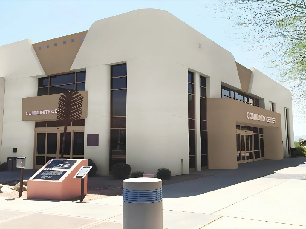 Exterior view of a modern beige community center with large windows and a sign that reads 'Community Center' above the entrance in the right wing.