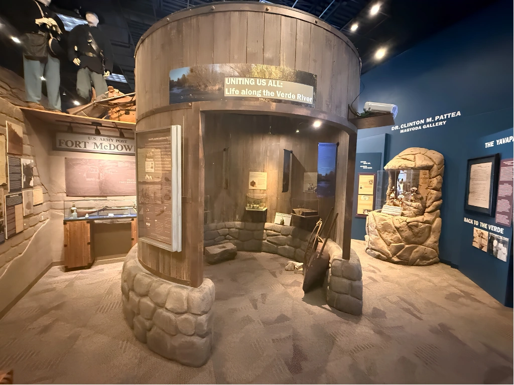 Interior museum exhibit: a circular wooden bunker with sandbag supports, conveying life along the Verde River.